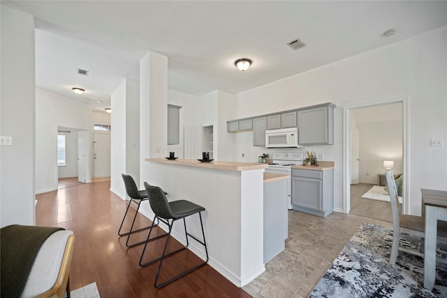 kitchen featuring visible vents, a kitchen bar, gray cabinets, white appliances, and light countertops