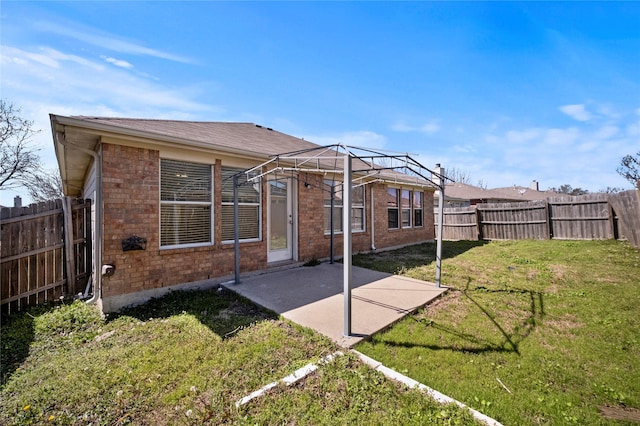 back of house featuring brick siding, a fenced backyard, a yard, and a patio