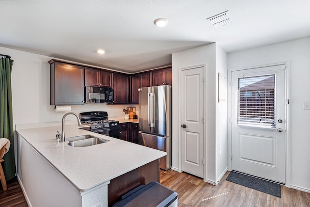 kitchen featuring light wood finished floors, visible vents, a peninsula, black appliances, and a sink