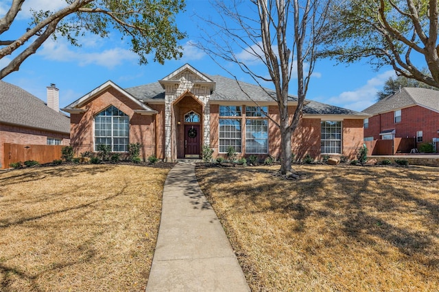 view of front of house with brick siding, a shingled roof, a front lawn, and fence