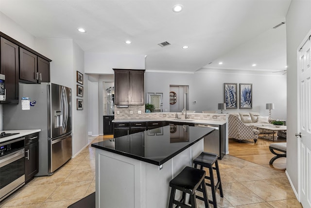 kitchen with a breakfast bar, a peninsula, stainless steel appliances, decorative backsplash, and open floor plan