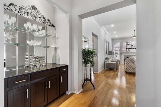 bar featuring light wood-style flooring, ornamental molding, wet bar, a fireplace, and baseboards