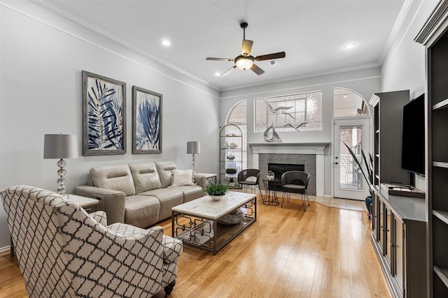 living room featuring light wood-type flooring, crown molding, and a tiled fireplace