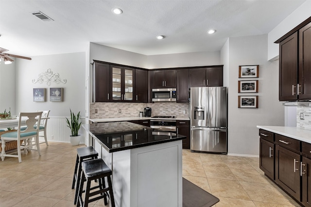 kitchen with dark brown cabinetry, appliances with stainless steel finishes, a kitchen bar, and light tile patterned flooring