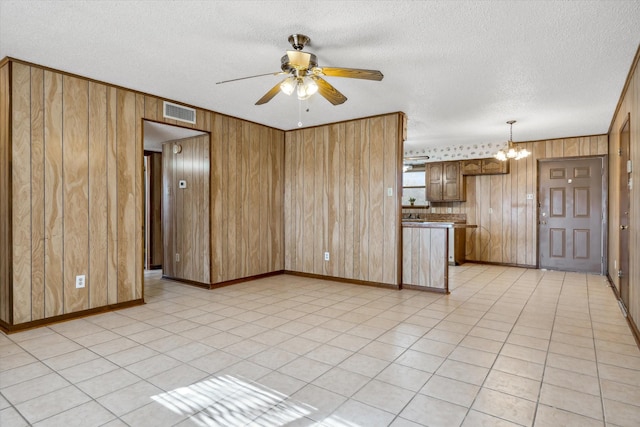 unfurnished living room with visible vents, wood walls, light tile patterned floors, ceiling fan with notable chandelier, and a textured ceiling