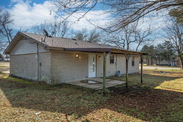 back of property featuring a patio, a lawn, brick siding, and roof with shingles