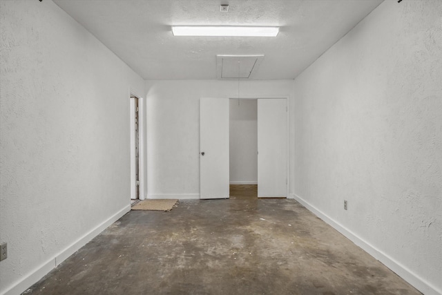 empty room with attic access, concrete floors, baseboards, and a textured wall