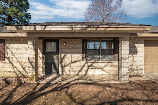 view of exterior entry with brick siding and an attached garage