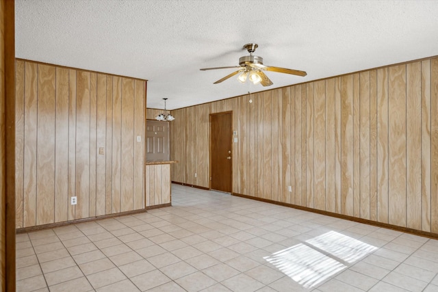 spare room with a textured ceiling, baseboards, wooden walls, and ceiling fan with notable chandelier