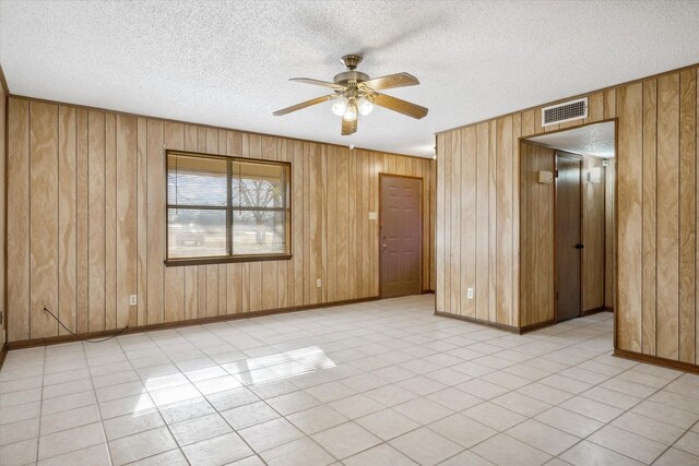 unfurnished room featuring ceiling fan, visible vents, wood walls, and a textured ceiling