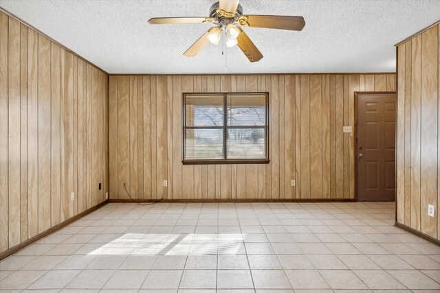 unfurnished room with wooden walls, light tile patterned floors, baseboards, ceiling fan, and a textured ceiling