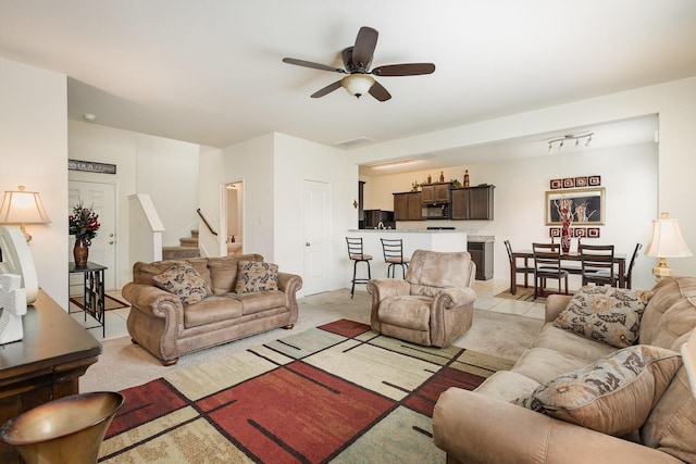 living area featuring light tile patterned floors, visible vents, ceiling fan, and stairs