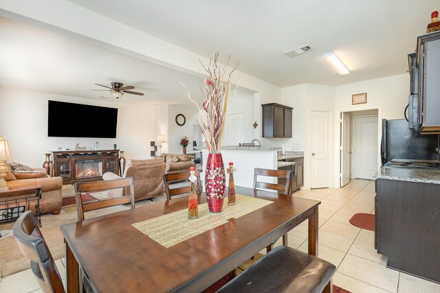 dining area featuring light tile patterned floors, visible vents, a ceiling fan, and a glass covered fireplace