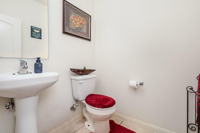 half bath featuring a sink, baseboards, toilet, and tile patterned flooring