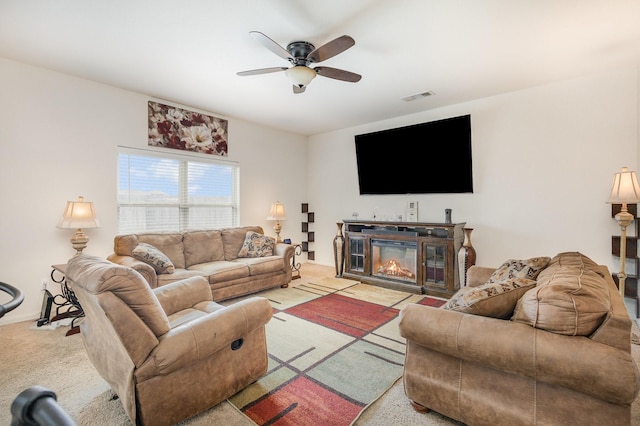 carpeted living area with a glass covered fireplace, visible vents, and ceiling fan