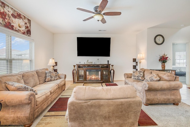 tiled living area with a glass covered fireplace, plenty of natural light, visible vents, and ceiling fan