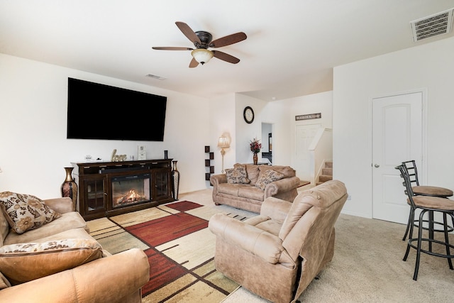 living area with visible vents, light colored carpet, a ceiling fan, and stairway