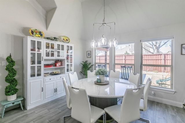 dining space featuring light wood finished floors, high vaulted ceiling, and baseboards