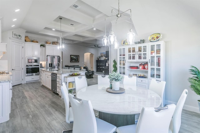 dining room featuring arched walkways, visible vents, coffered ceiling, and light wood-style floors