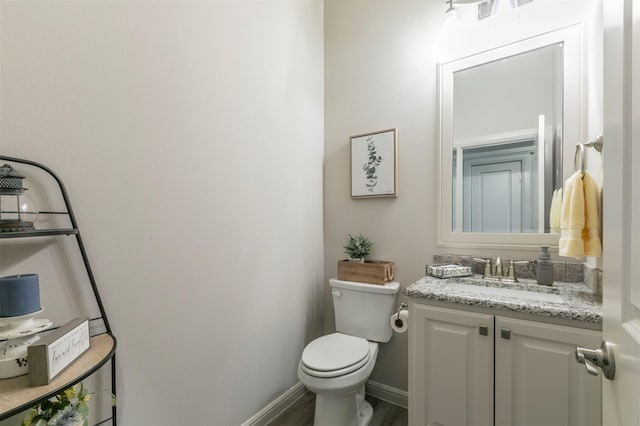 half bathroom featuring vanity, toilet, and baseboards