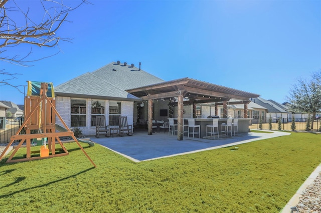 back of property with fence, roof with shingles, a playground, a patio area, and outdoor dry bar