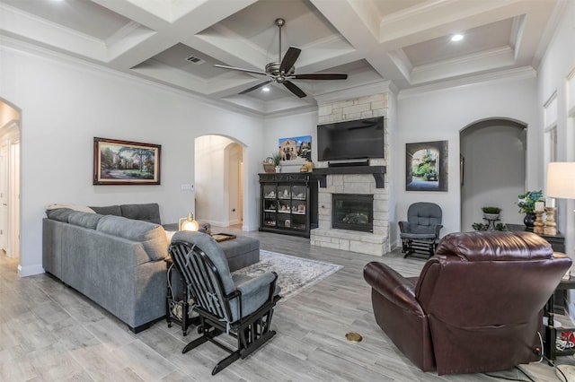 living area with coffered ceiling, arched walkways, ceiling fan, a stone fireplace, and beamed ceiling