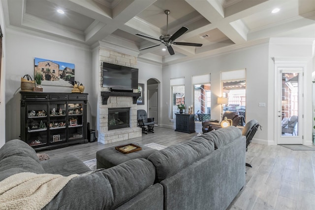 living room featuring beamed ceiling, wood finished floors, a stone fireplace, and ceiling fan