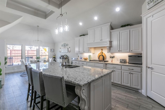 kitchen with an island with sink, a sink, a kitchen breakfast bar, white cabinets, and light stone countertops