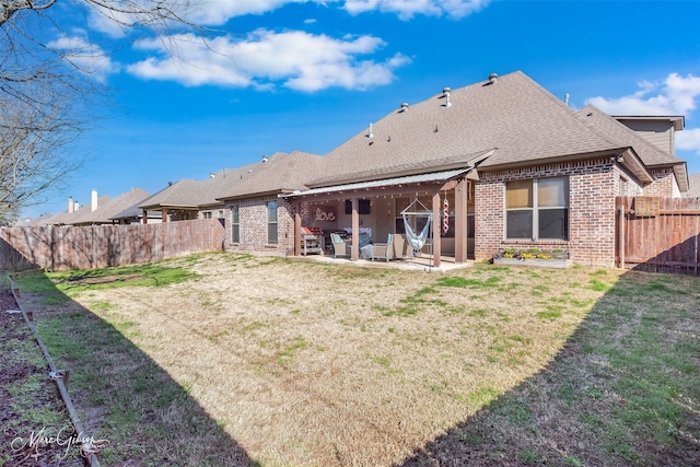 back of property featuring a lawn, a patio, a fenced backyard, a shingled roof, and brick siding