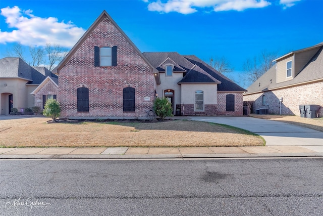 view of front of property with brick siding, central air condition unit, a front yard, stucco siding, and driveway