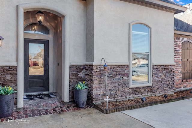 property entrance with stone siding, stucco siding, and a shingled roof