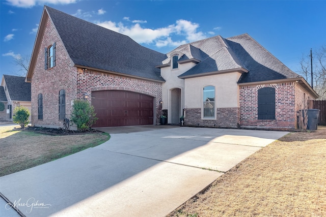 french country style house with brick siding, roof with shingles, concrete driveway, and a front lawn