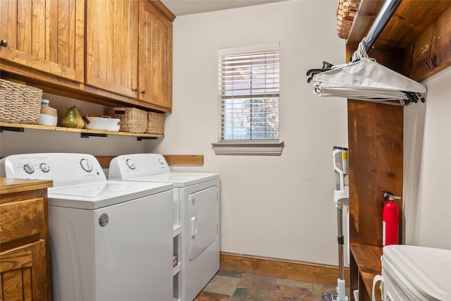 clothes washing area with cabinet space, washing machine and dryer, baseboards, and stone finish floor