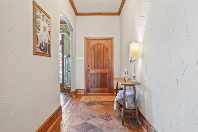 foyer featuring baseboards, arched walkways, ornamental molding, and stone finish floor