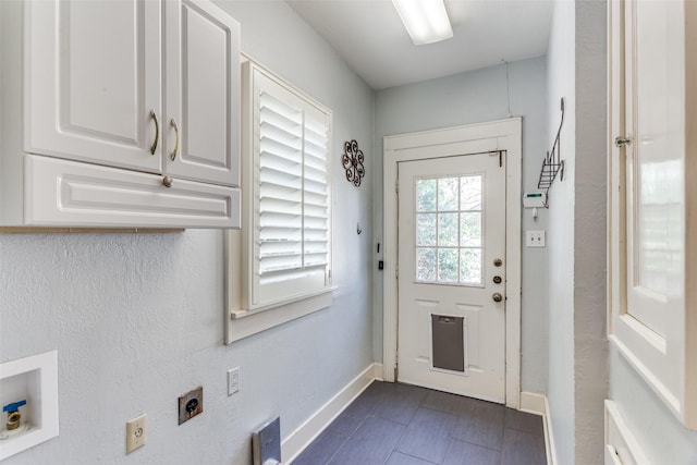 doorway with baseboards and dark tile patterned flooring