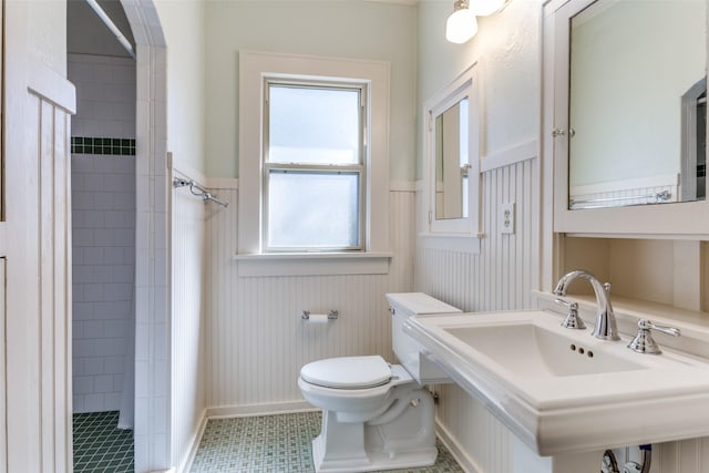 full bathroom featuring a sink, a wainscoted wall, tiled shower, and toilet