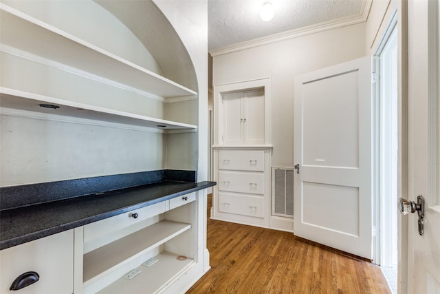 unfurnished office featuring visible vents, a textured ceiling, crown molding, and wood finished floors