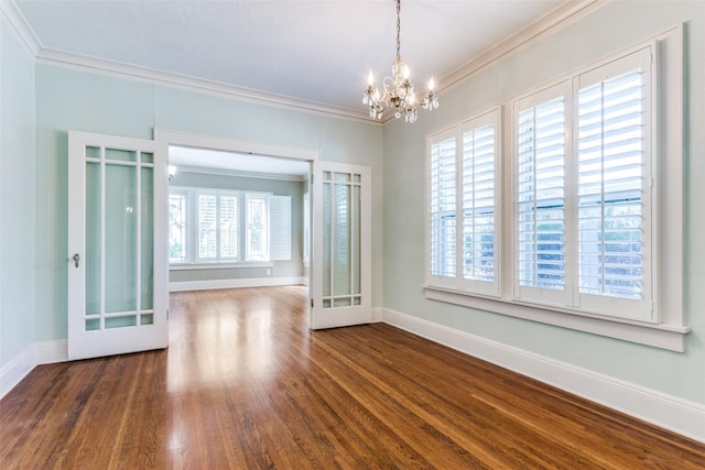 spare room featuring baseboards, an inviting chandelier, wood finished floors, and crown molding