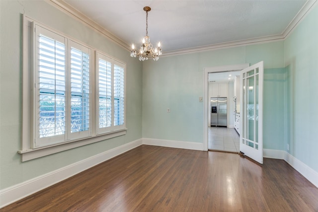 empty room featuring crown molding, wood finished floors, baseboards, and a chandelier