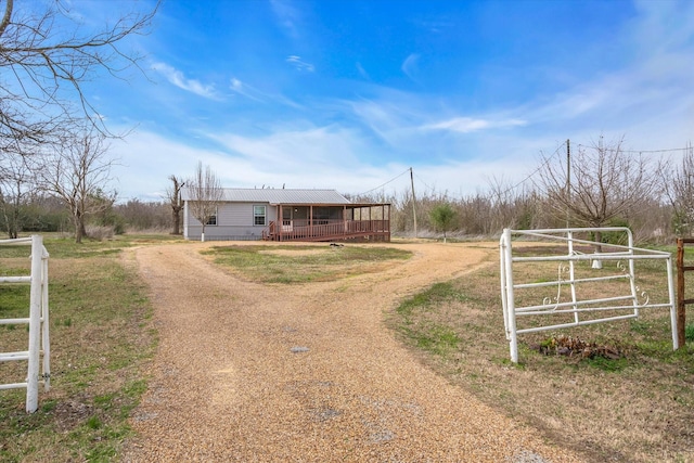 view of front facade with a wooden deck, a rural view, driveway, and a gate