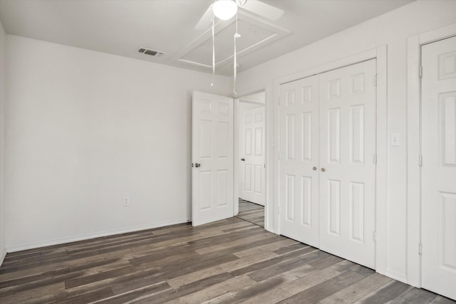 unfurnished bedroom featuring visible vents, wood finished floors, a closet, attic access, and ceiling fan