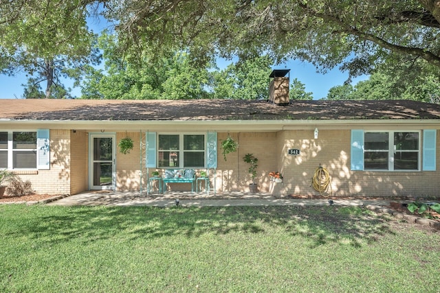 ranch-style house with brick siding, a chimney, and a front yard