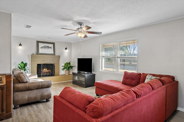 living room featuring visible vents, ceiling fan, a textured ceiling, a brick fireplace, and light wood-type flooring