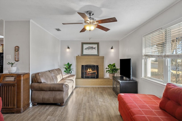 living room with crown molding, a brick fireplace, wood finished floors, and visible vents