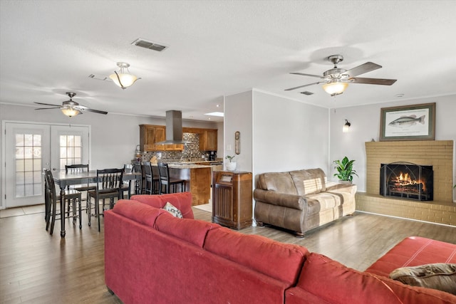 living area with ceiling fan, visible vents, a brick fireplace, and light wood-style flooring