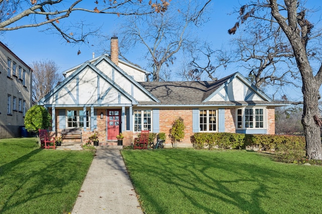 tudor-style house with a front lawn, brick siding, roof with shingles, and a chimney