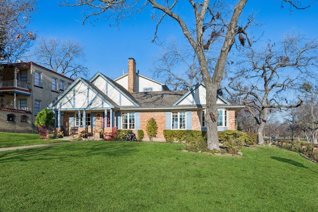 view of front facade featuring a front lawn, brick siding, roof with shingles, and a chimney