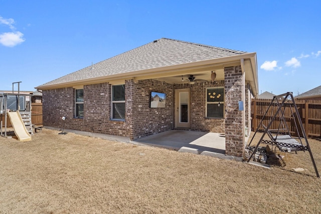 rear view of house featuring a ceiling fan, fence, roof with shingles, a playground, and a patio area