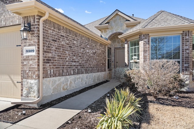 view of side of home featuring brick siding, stone siding, an attached garage, and a shingled roof