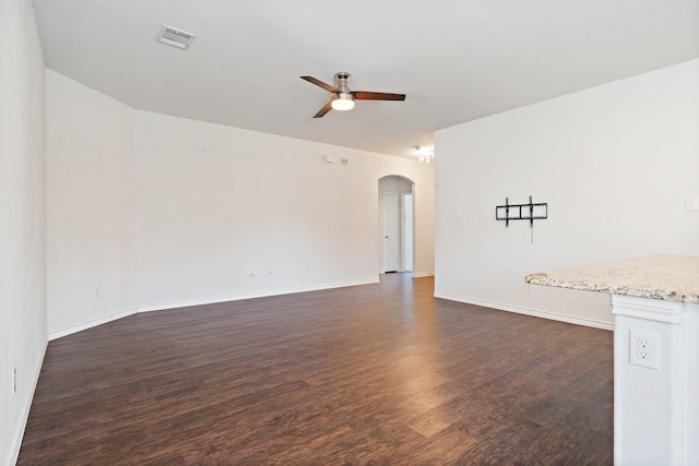 empty room with visible vents, a ceiling fan, dark wood finished floors, arched walkways, and baseboards